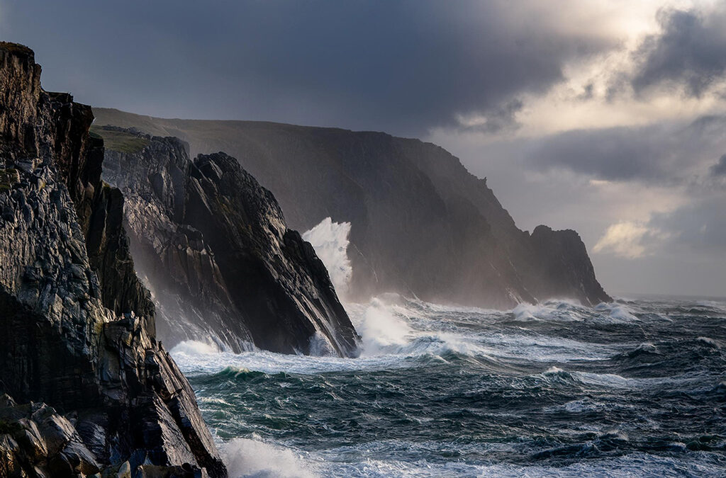 Rugged coastal cliffs battered by stormy waves under a brooding sky, capturing the atmosphere of The Bastion of Broken Kings.