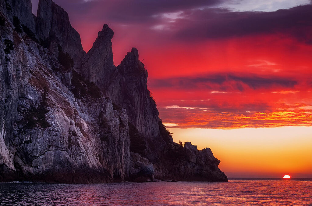 Dramatic sunset over Scarlet Ridge with jagged cliffs and vibrant red and purple sky.